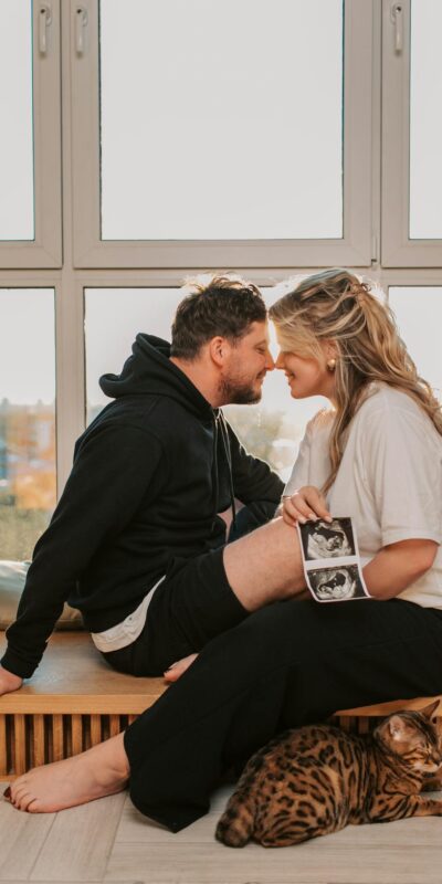 A couple sharing a tender moment with a Bengal cat and sonogram in a sunny room.