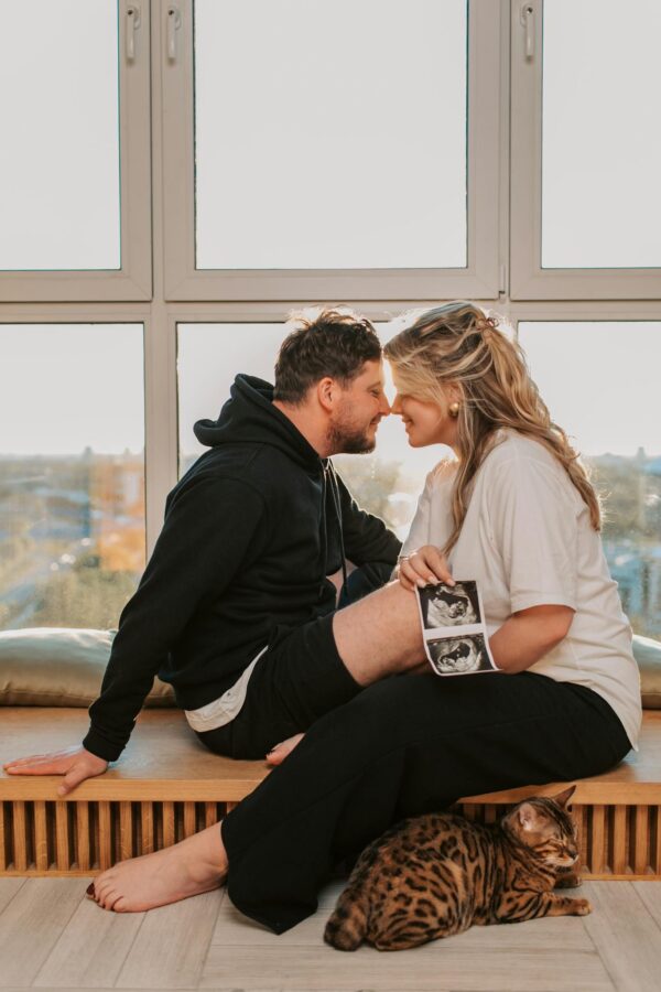 A couple sharing a tender moment with a Bengal cat and sonogram in a sunny room.